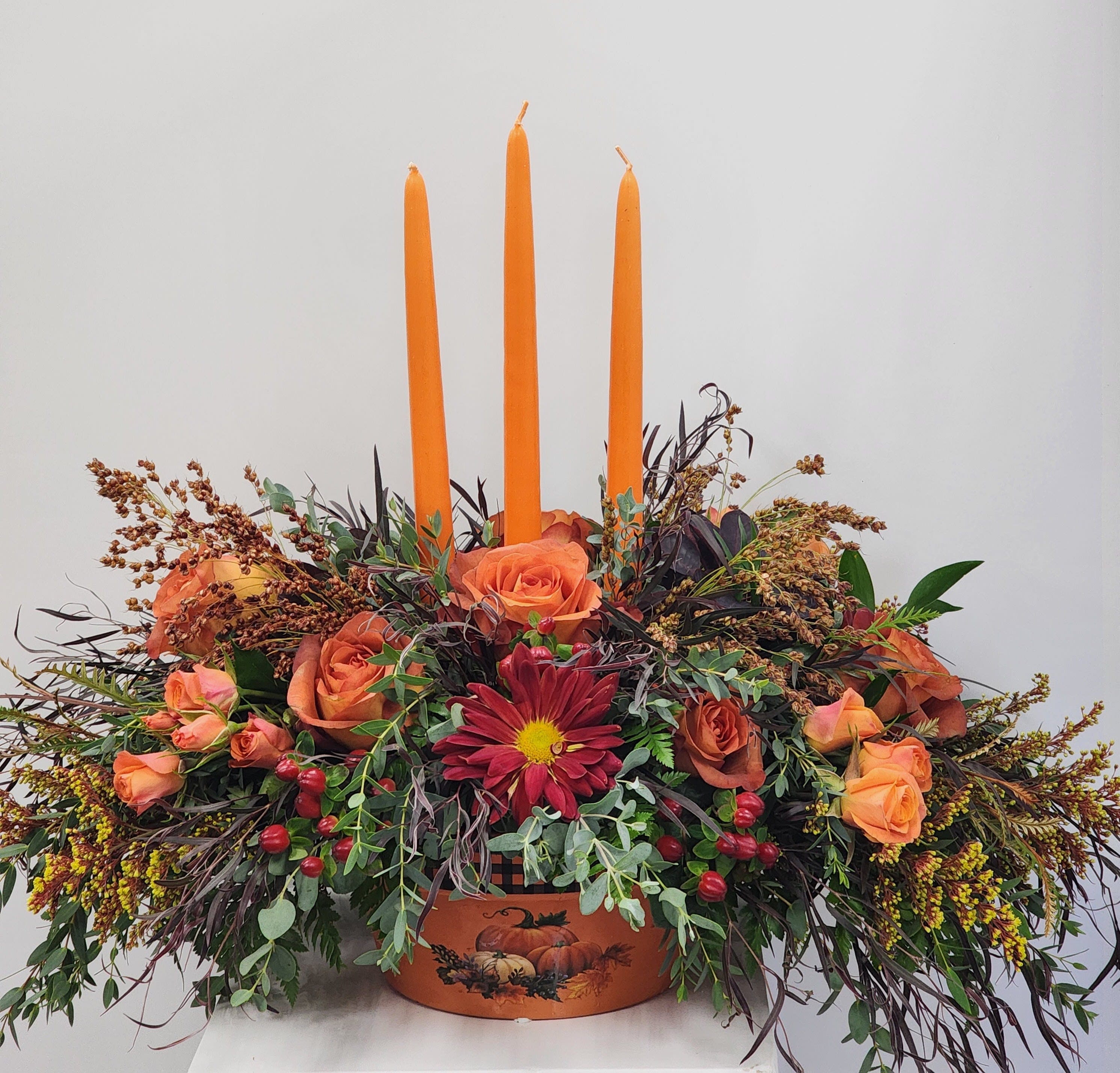 Feast Florals Centerpiece - A colorful orange and plaid ceramic dish centerpiece for a 8-10 person table. Filled with roses, spray roses, chrysanthemums, broomcorn, hypericum, and solidago.  Approximately 18" tall by 26" long.