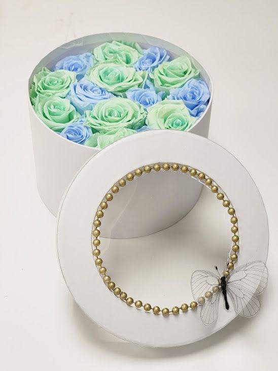 Round box of pastel roses with a gold beaded lid and butterfly accent