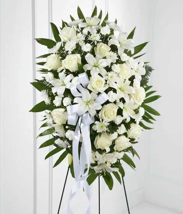 Exquisite Tribute Standing Spray - The FTD Exquisite Tribute Standing Spray is an elegant display of sweet serenity. White roses, Asiatic lilies, chrysanthemums and mini carnations are artfully arranged amongst emerald palm fronds and lush greens. Accented by white satin ribbon and standing on a wire easel, this standing spray is an outstanding way to honor the life of your loved one. FTD S4447p  To allow for the freshest blooms possible, we may substitute for a different variety or color of flower.