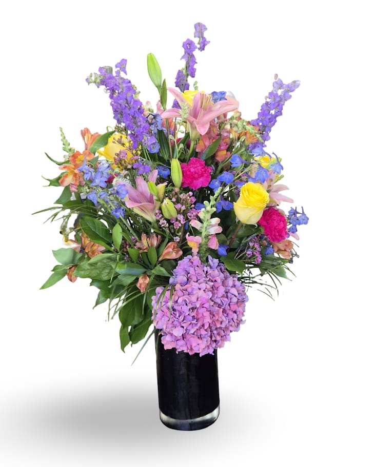 Colorful mixed bouquet in a black vase with lilies, roses, and purple blooms