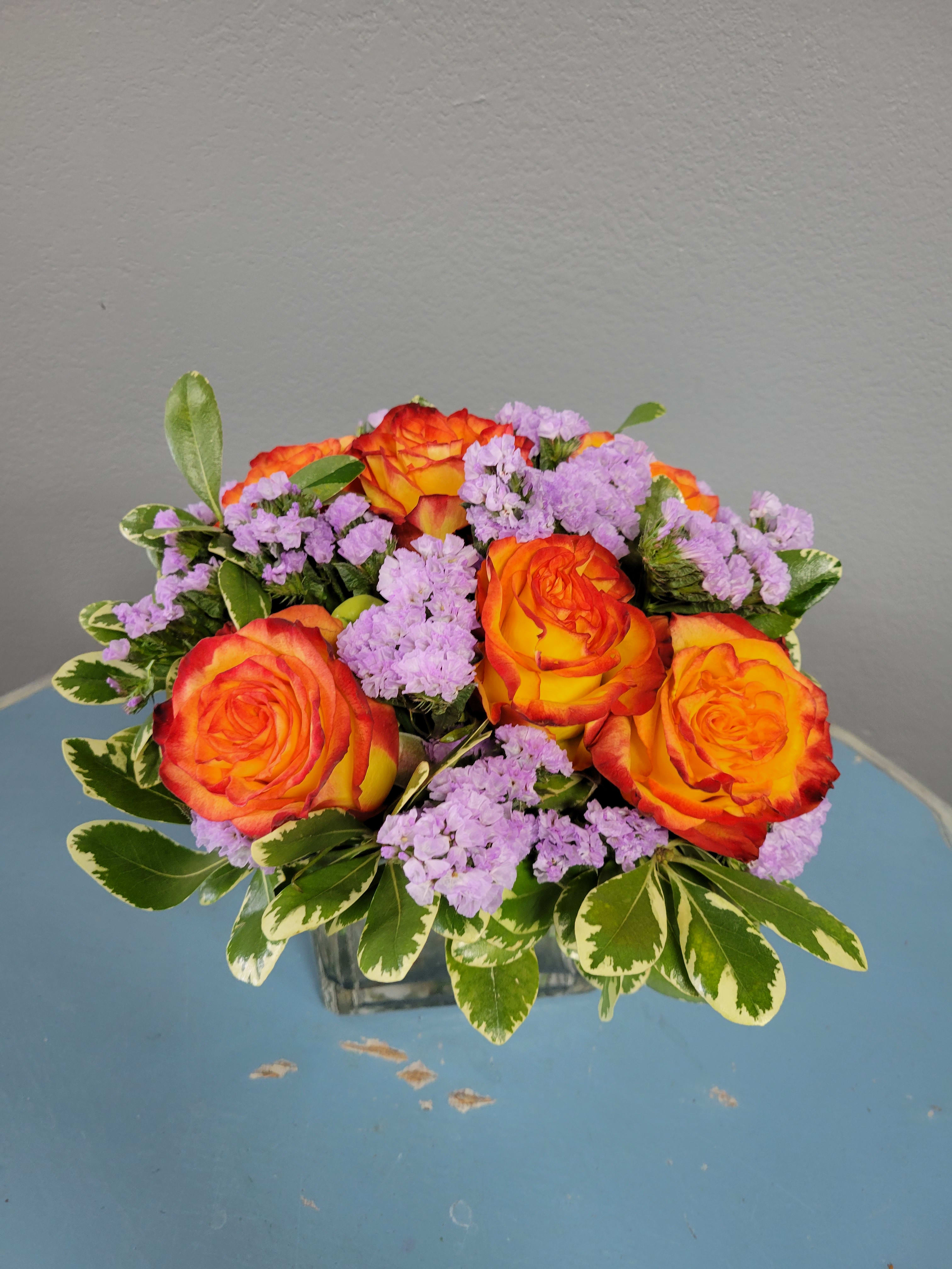Orange roses and lavender filler flowers in a square glass vase