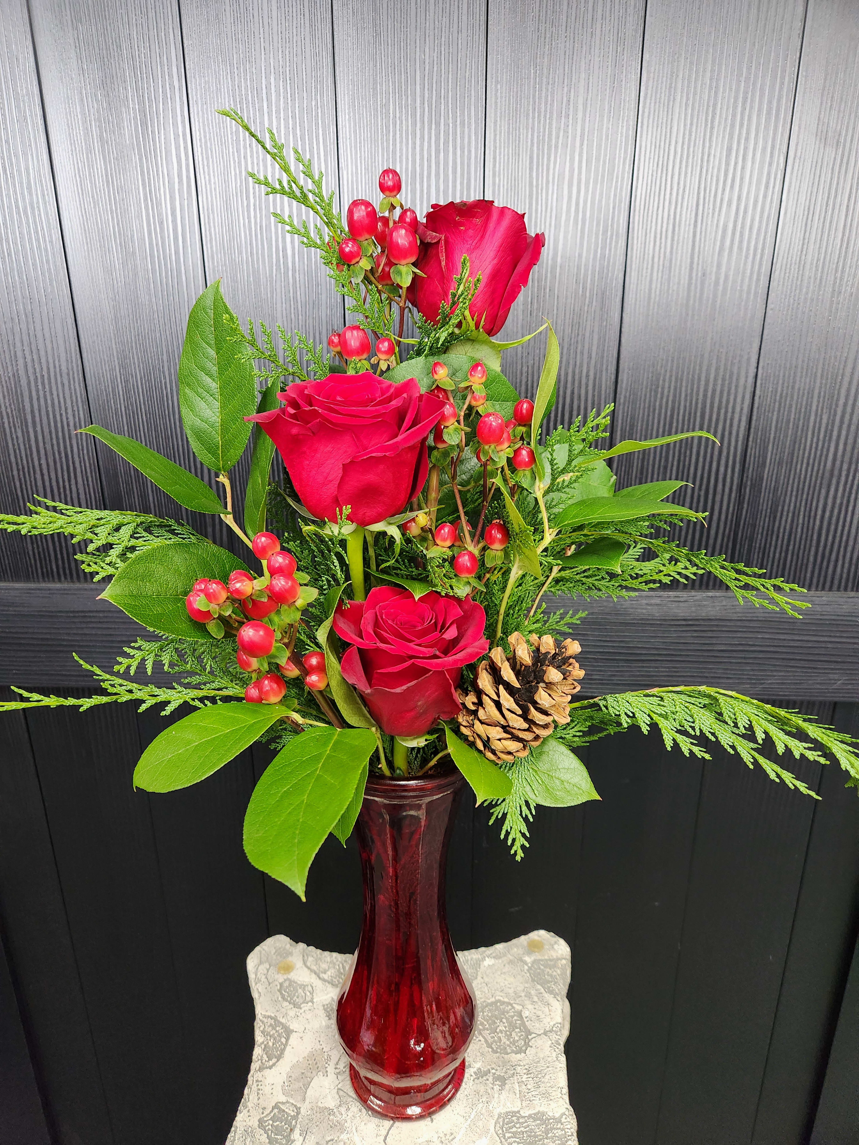 Red roses arranged in a red vase with berries and a pinecone