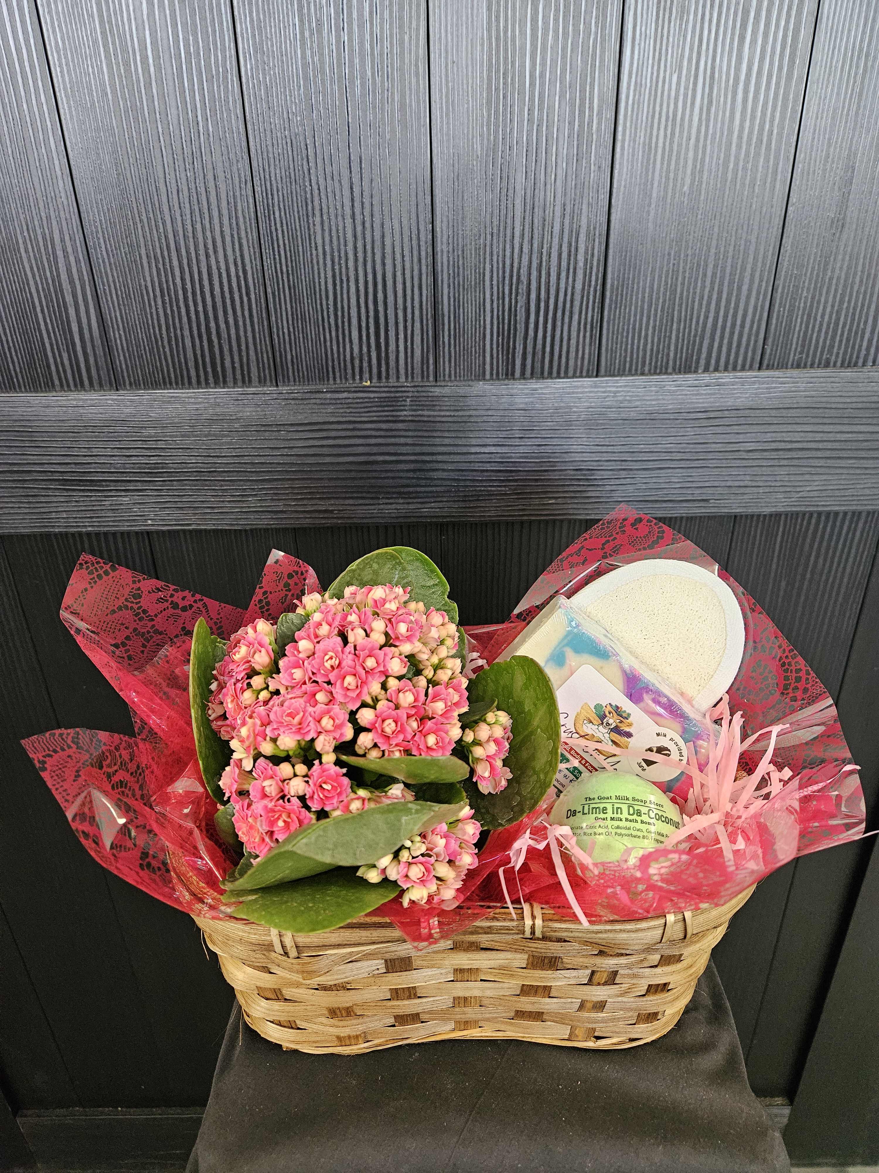 Pink flowering plant in a wicker basket with bath gift items