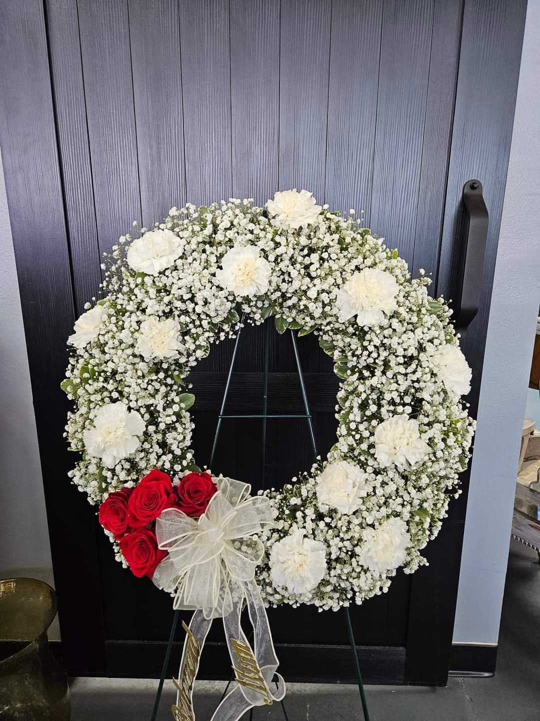 White floral wreath with red roses and a sheer bow on a stand
