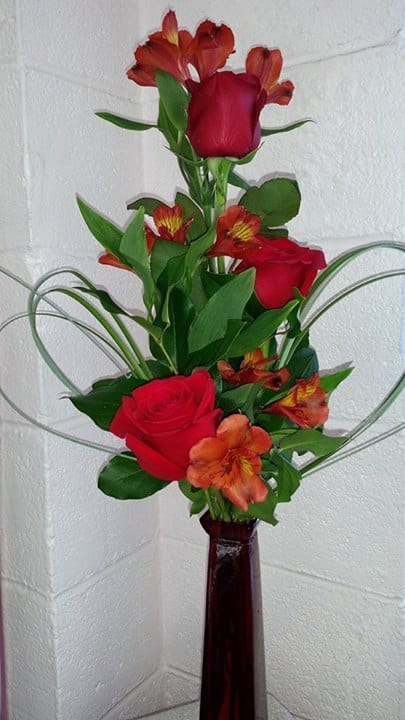 Red roses and orange alstroemeria in a tall vase arrangement