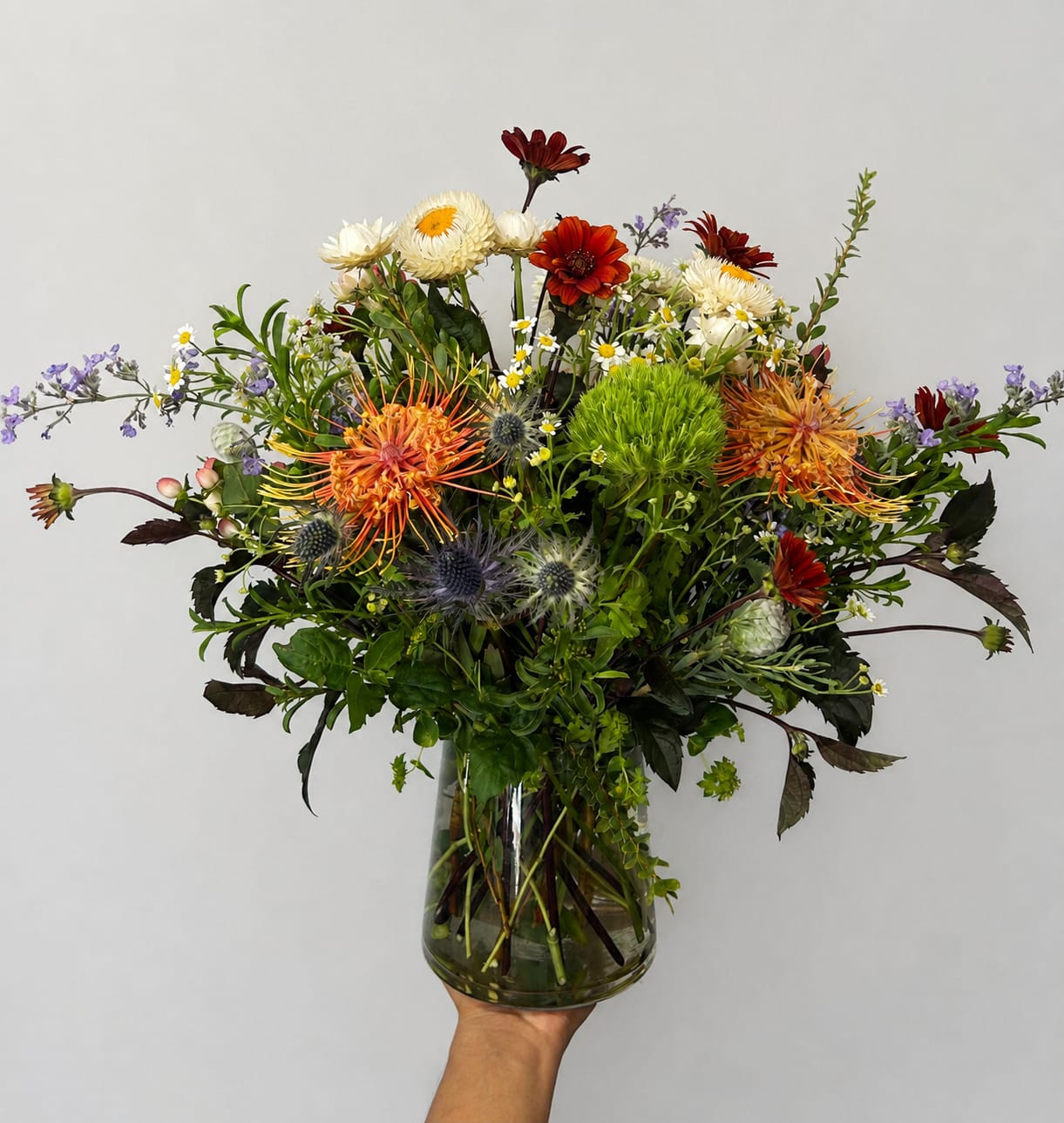 Mixed bouquet in a clear glass vase with orange, white, and red blooms