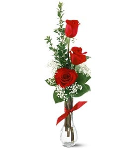 Three red roses in a clear glass vase with a red ribbon
