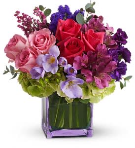 Mixed bouquet of roses, hydrangeas, and purple flowers in a purple glass vase