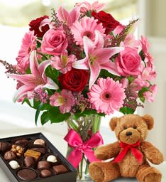 Pink and red mixed flower bouquet in a glass vase with a teddy bear and chocolates