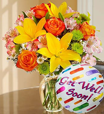 Bouquet of yellow lilies and orange roses in a glass vase with a "Get Well Soon" balloon