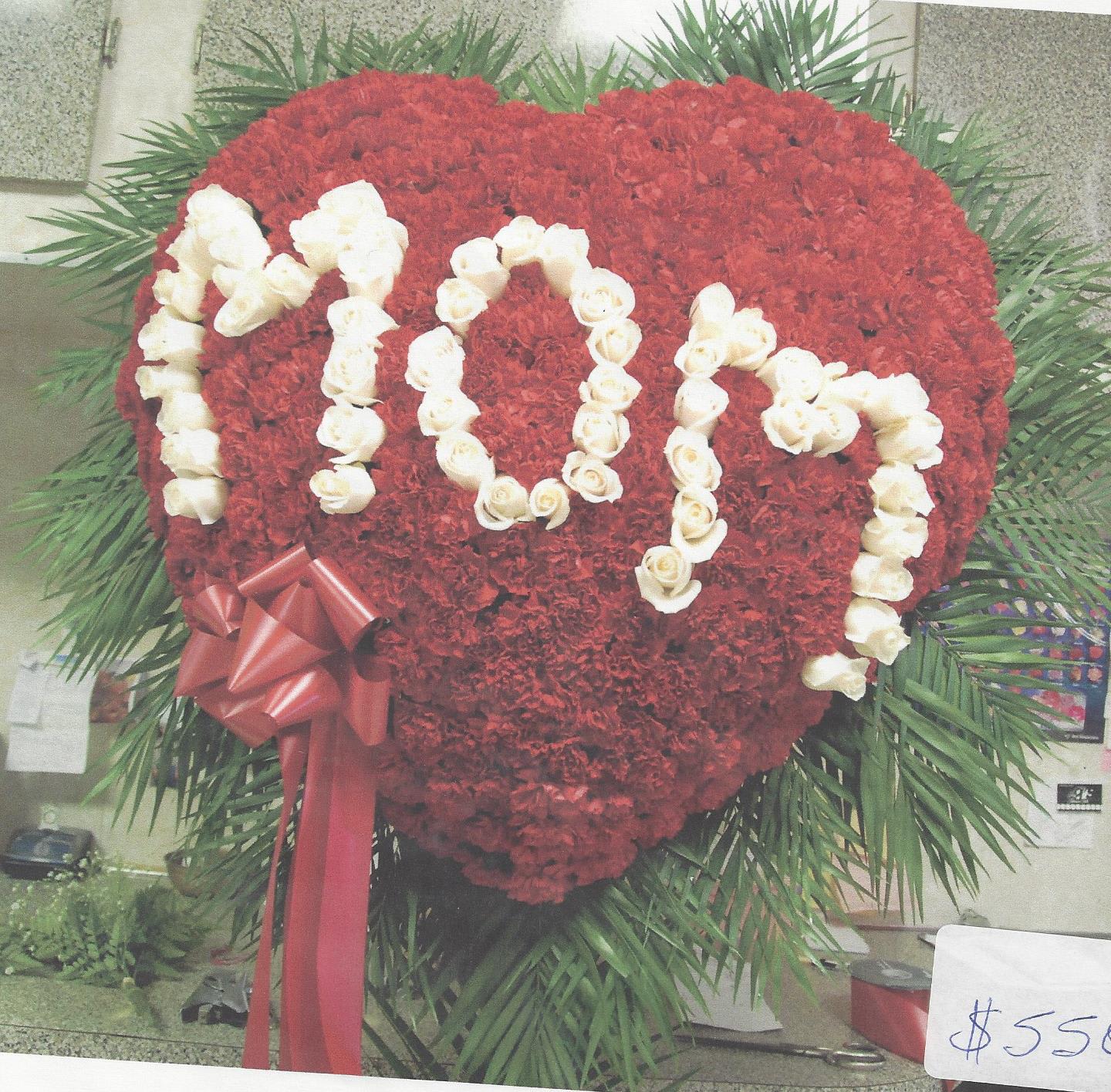 Heart-shaped red floral arrangement with white rose lettering and a red ribbon bow