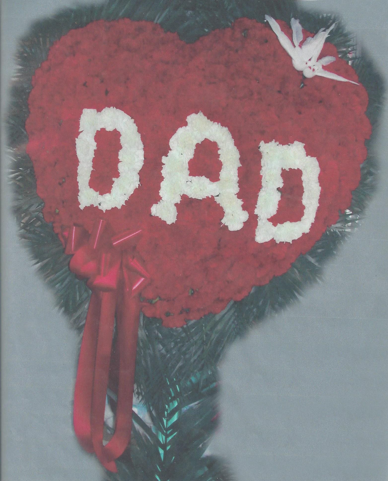 Heart-shaped red floral tribute with white letters and ribbon