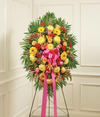 Standing floral spray with bright mixed flowers and a pink ribbon on an easel