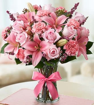 Pink lilies and roses arranged in a glass vase with a pink ribbon