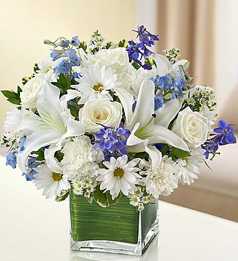 White lilies, roses, and daisies with blue flowers in a square glass vase