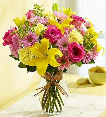 Bouquet of pink roses, yellow lilies, and pink daisies in a glass vase