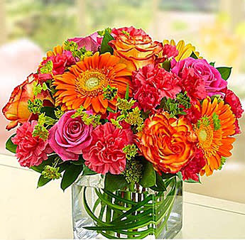 Bright mixed bouquet of orange, pink, and yellow flowers in a clear vase