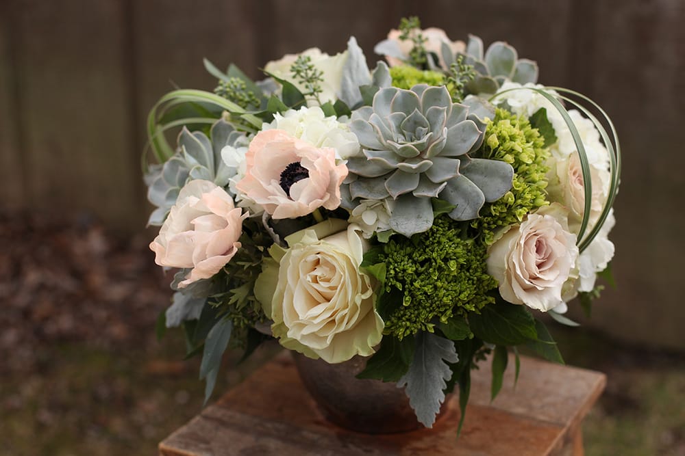 Soft pink and white flowers arranged with gray succulents in a bowl vase.