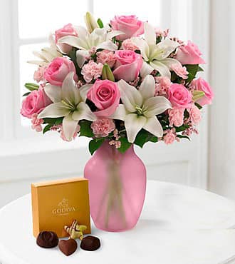 Pink roses and white lilies in a pink vase with a box of chocolates