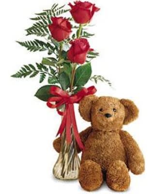 Three red roses in a vase beside a teddy bear