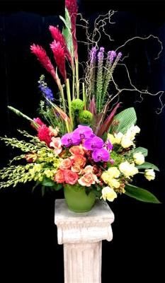 Tall mixed floral arrangement in a green vase with pink, purple, and white blooms