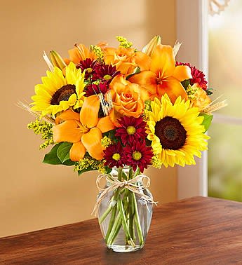 Bouquet of sunflowers, orange lilies, and red daisies in a glass vase