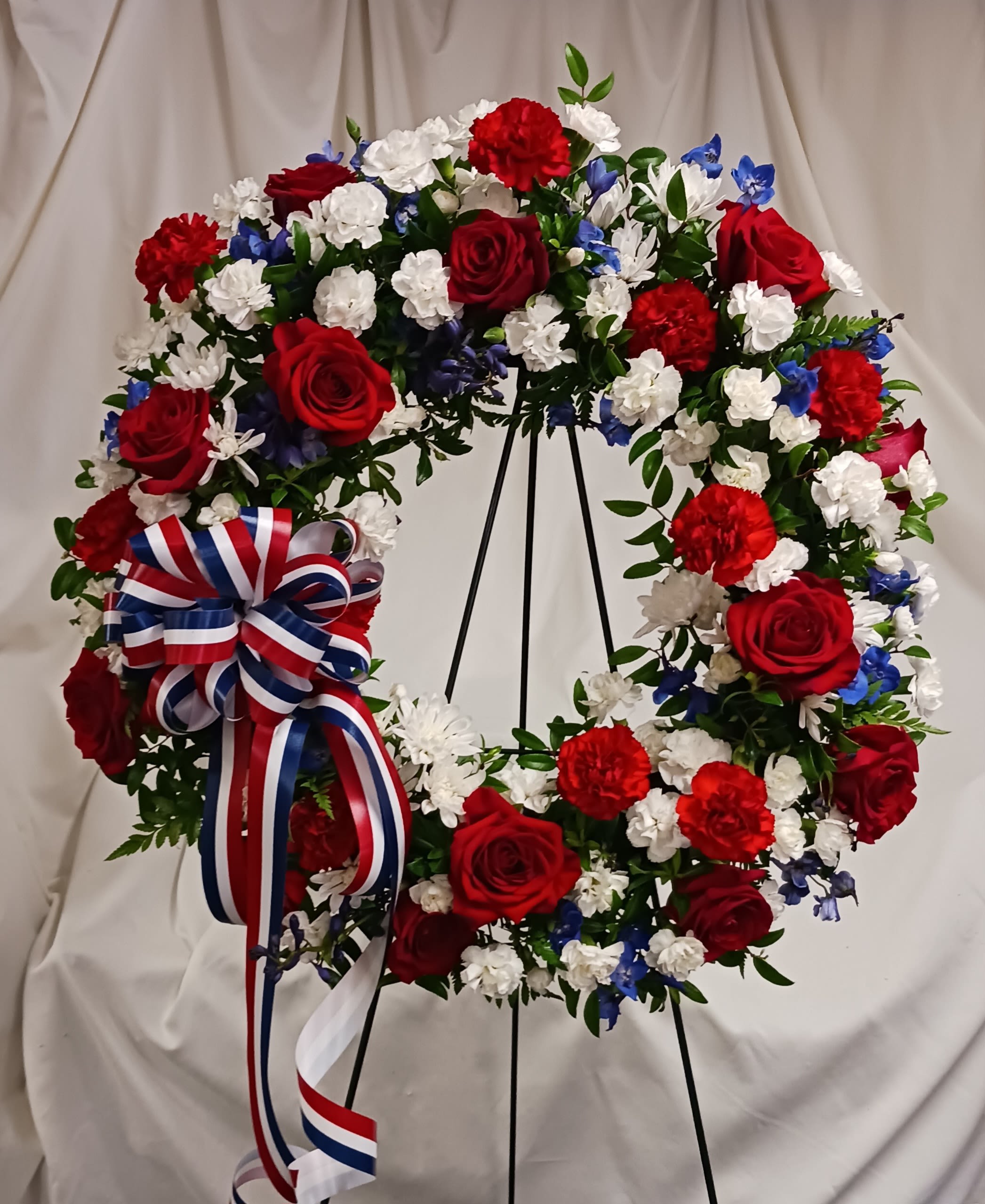 Circular wreath of red, white, and blue flowers on a stand with a ribbon bow