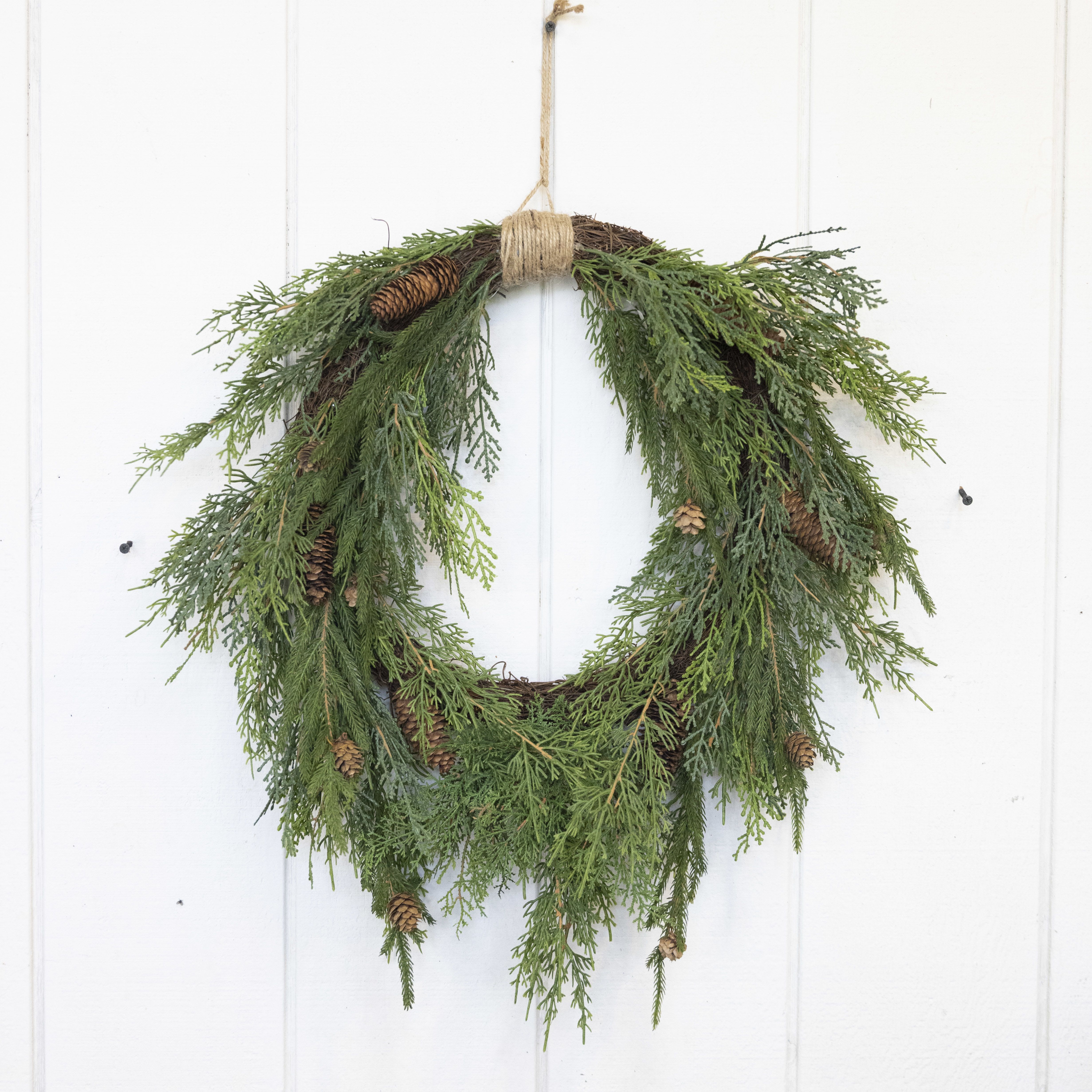 Evergreen wreath with pinecones hanging on a white door