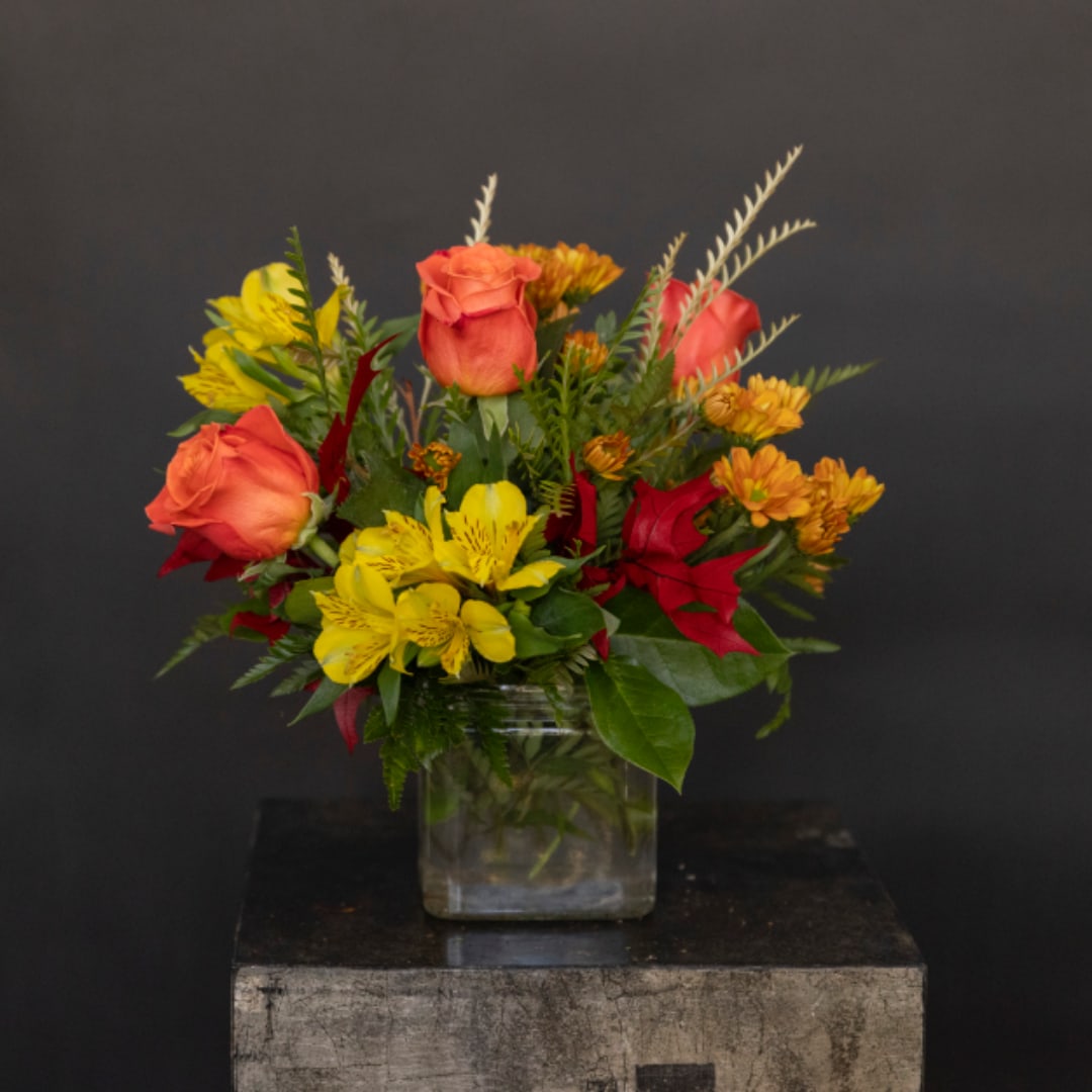 Mixed bouquet of orange roses and yellow flowers in a glass vase