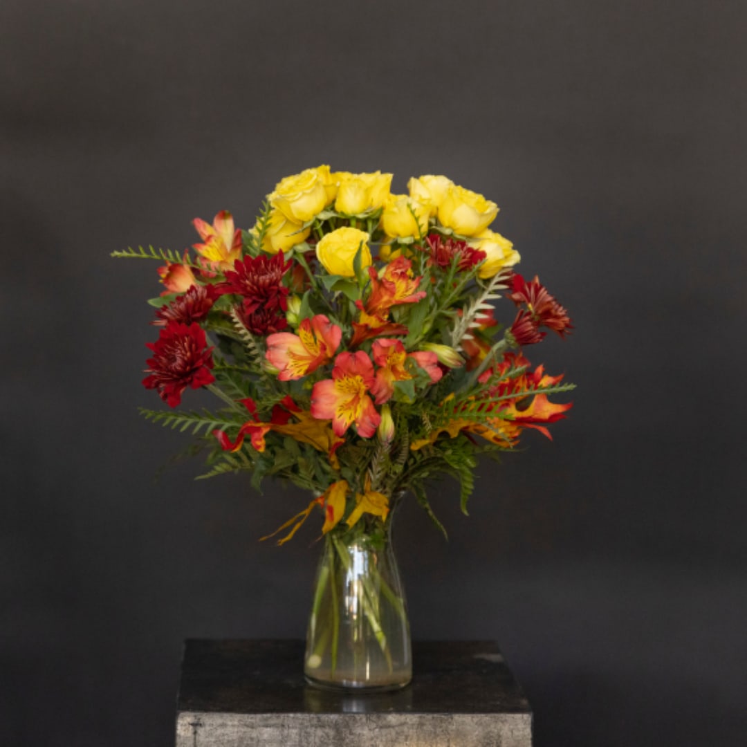 Yellow roses and red-orange flowers in a clear glass vase