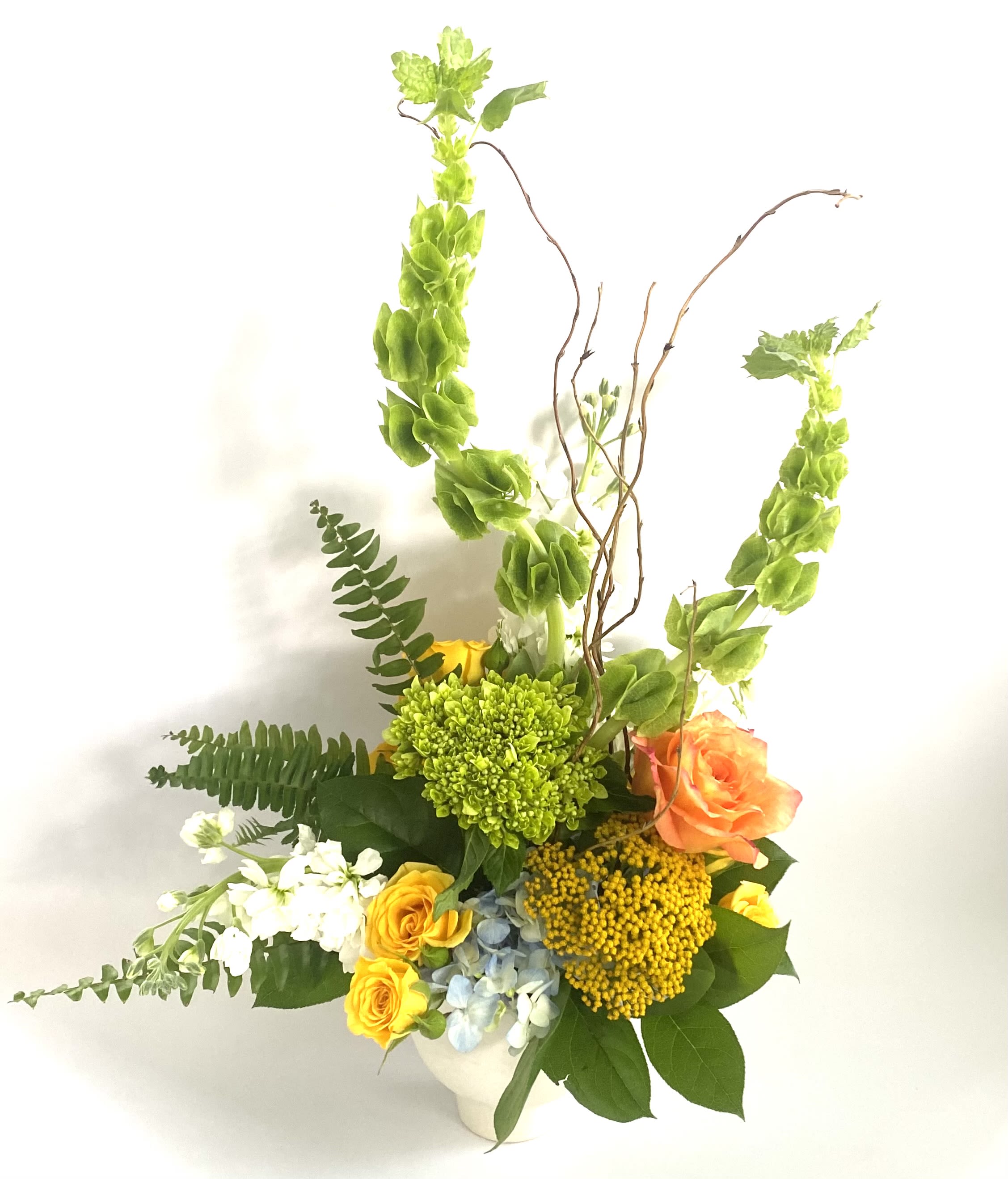 Tall mixed flower arrangement in a white vase with orange and yellow blooms