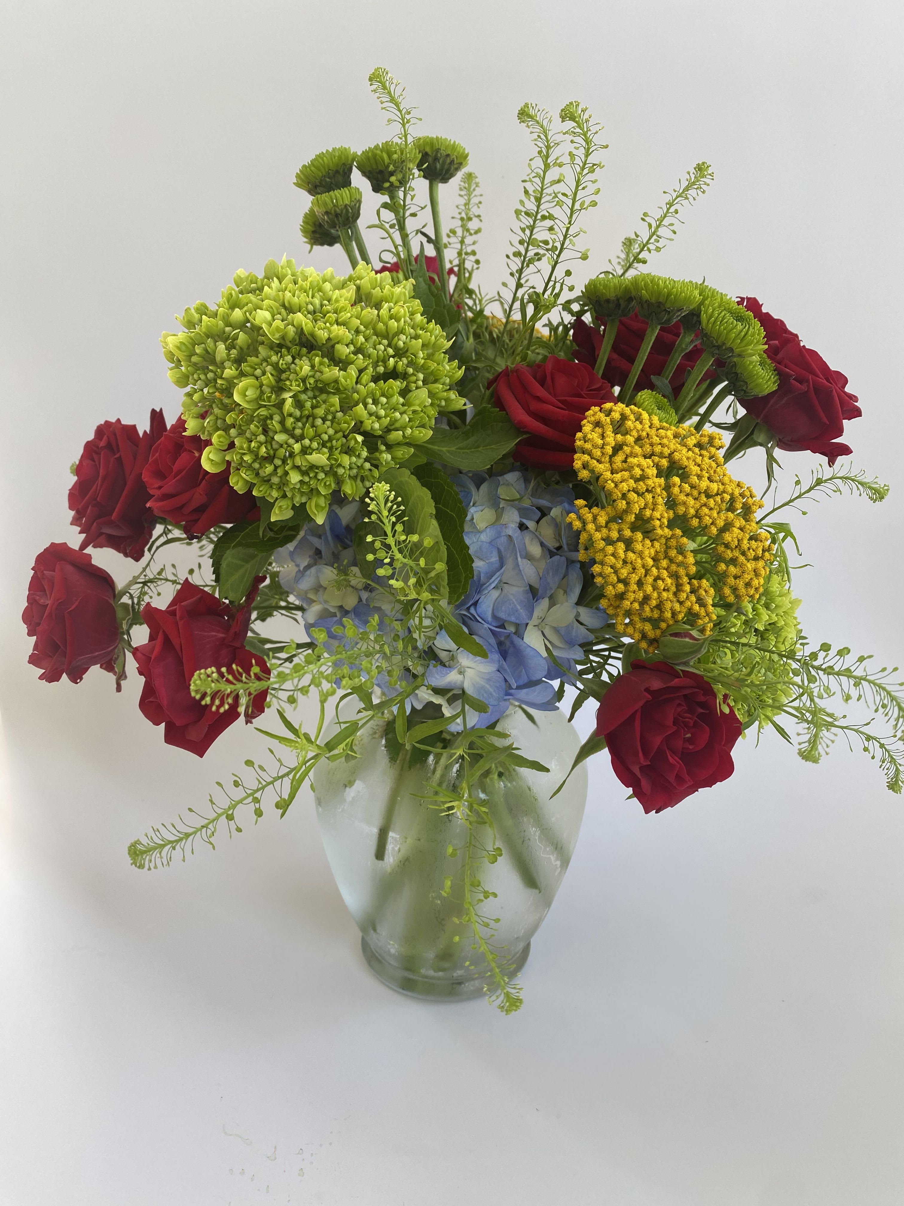 Mixed bouquet of red roses, blue hydrangea, and green chrysanthemums in a glass vase