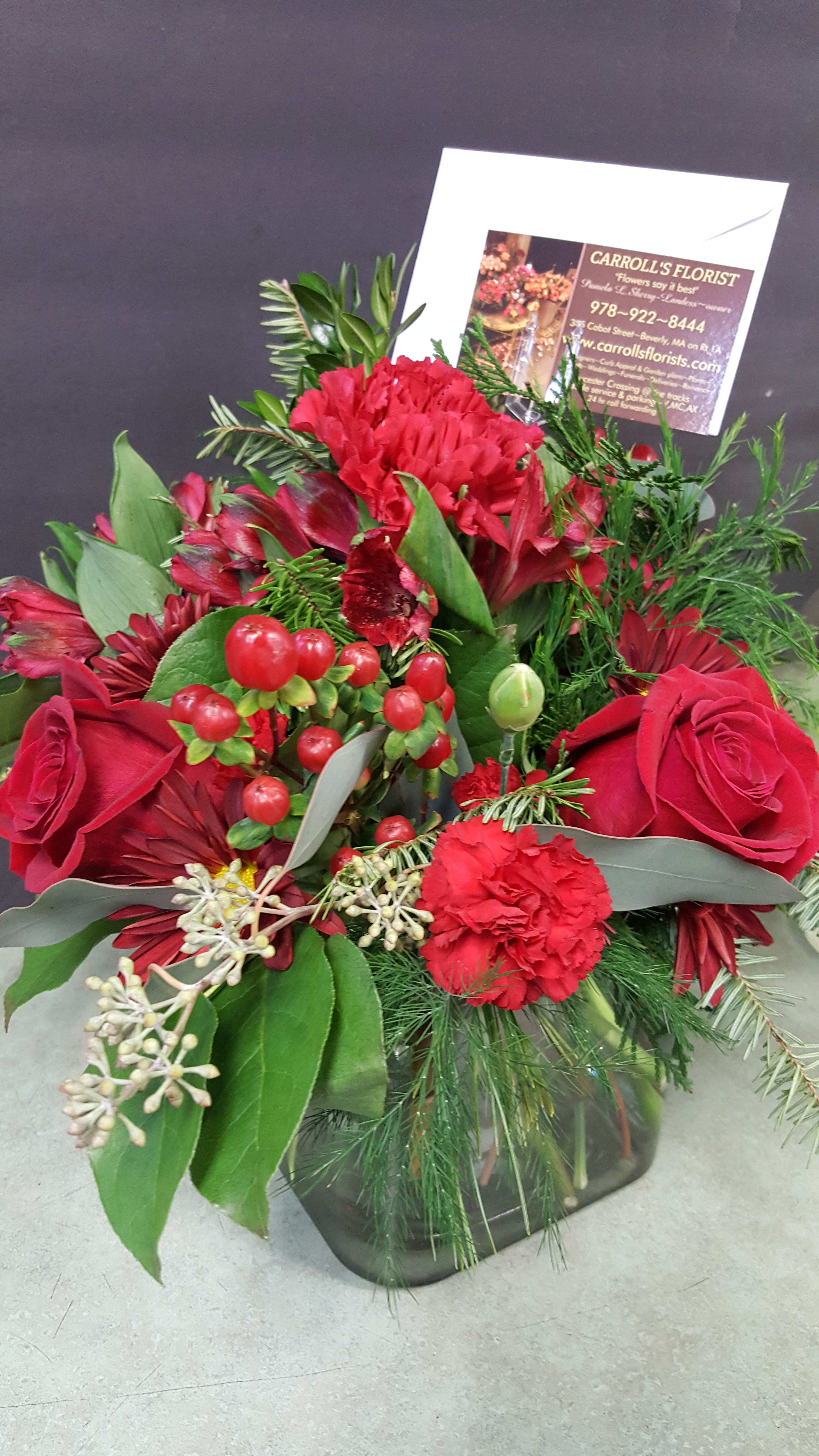 Red roses and carnations with berries in a square glass vase with a florist card