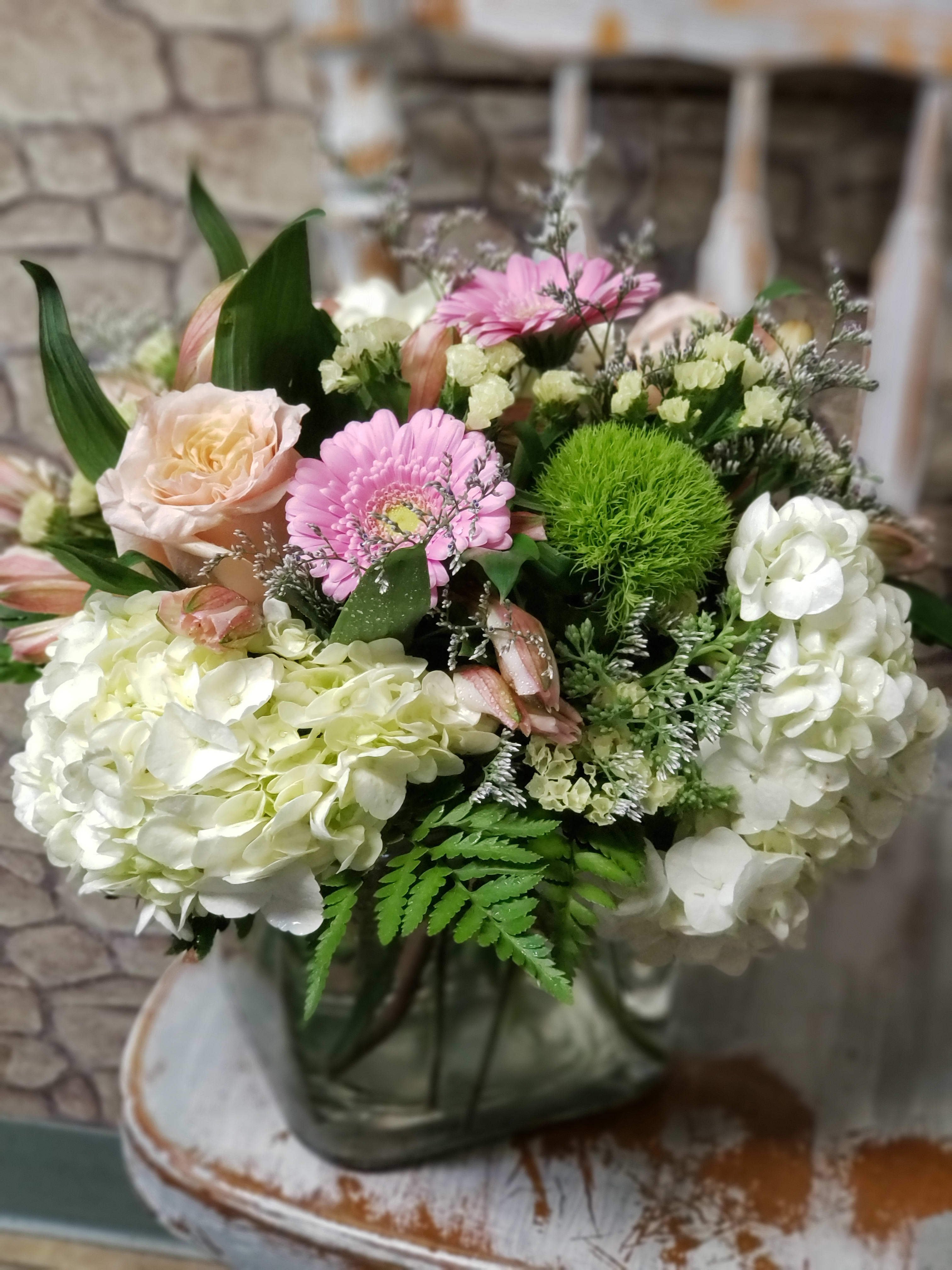 White hydrangeas with pink gerbera, peach rose, and green mums in a square glass vase