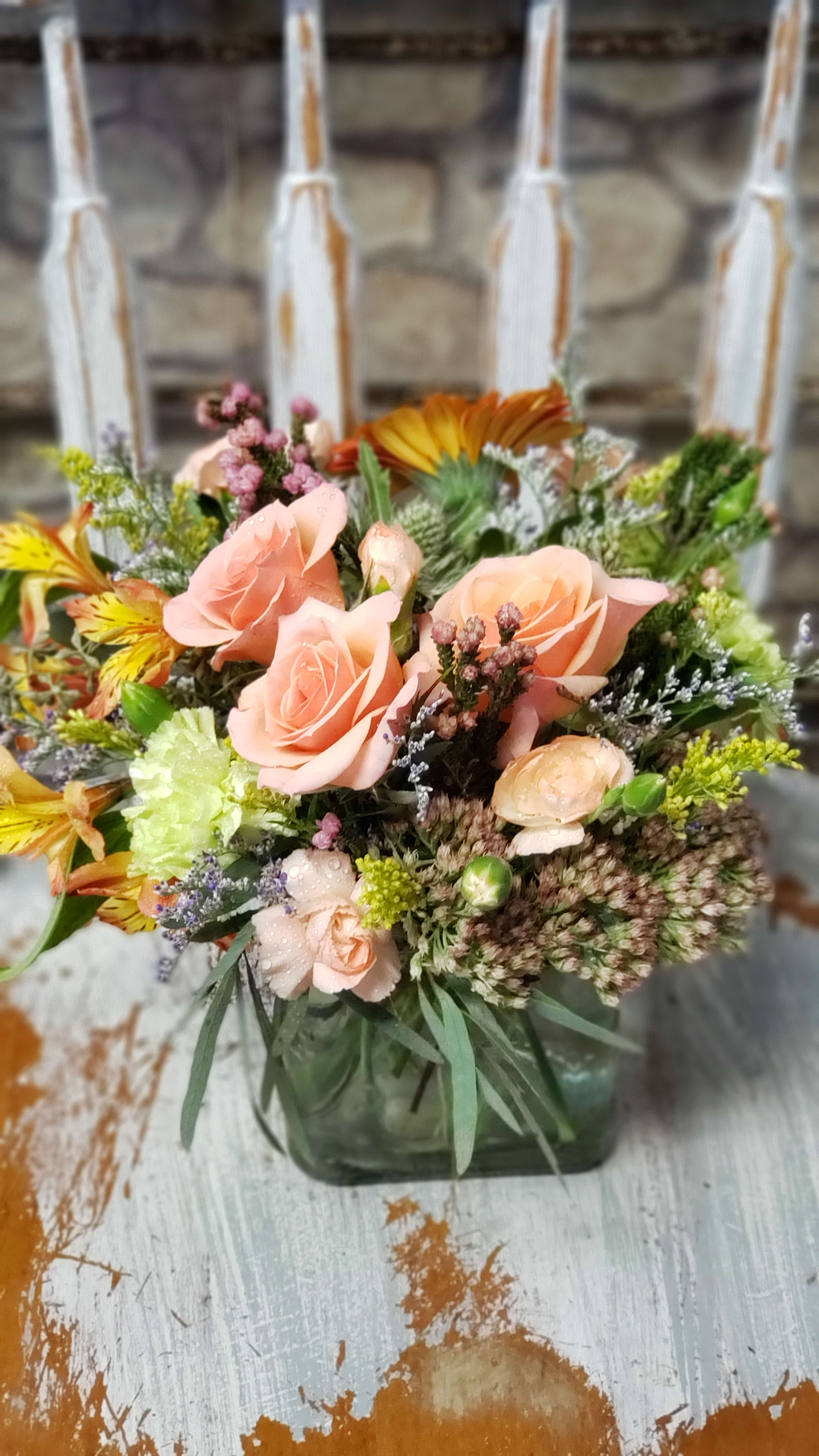 Peach roses and mixed flowers arranged in a square glass vase