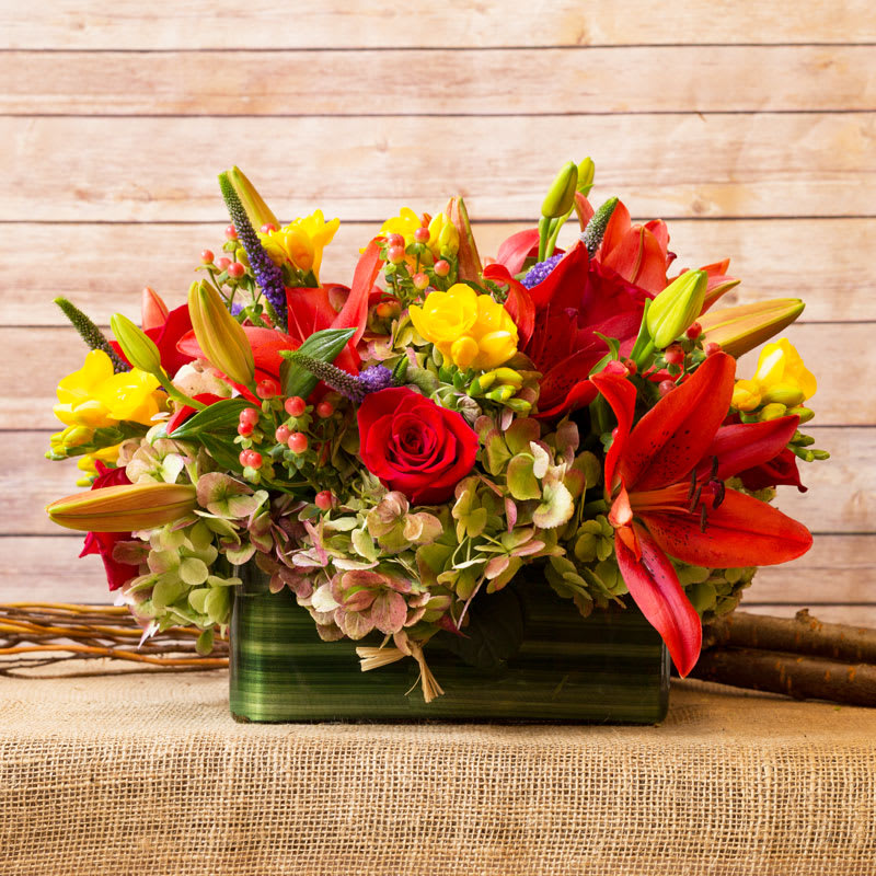OVAL CENTERPIECE  - MIXED SEASONAL SPRING FLOWERS ARRANGED IN OBLONG GLASS.
