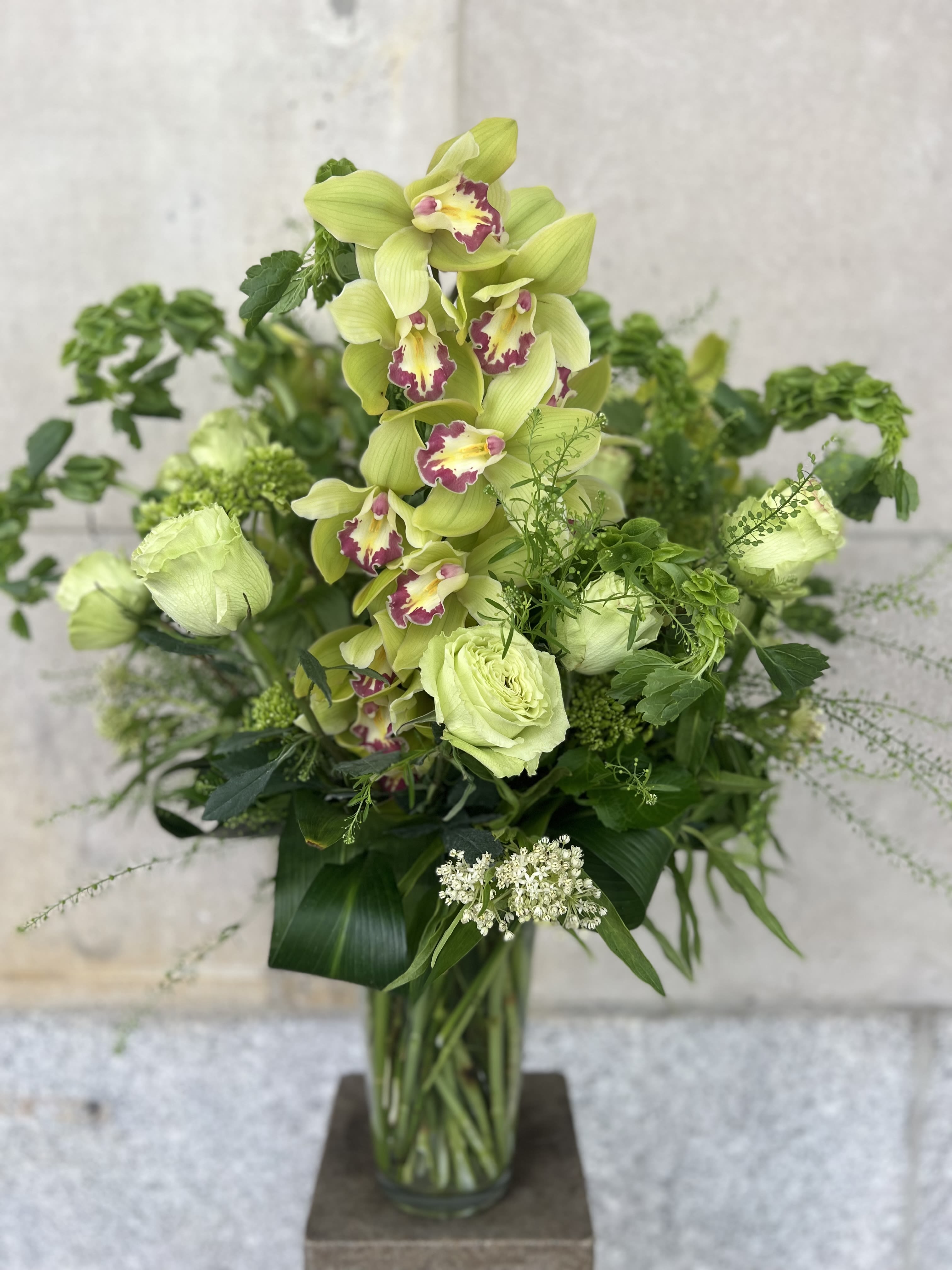 Tall green orchid arrangement in a glass vase with mixed foliage