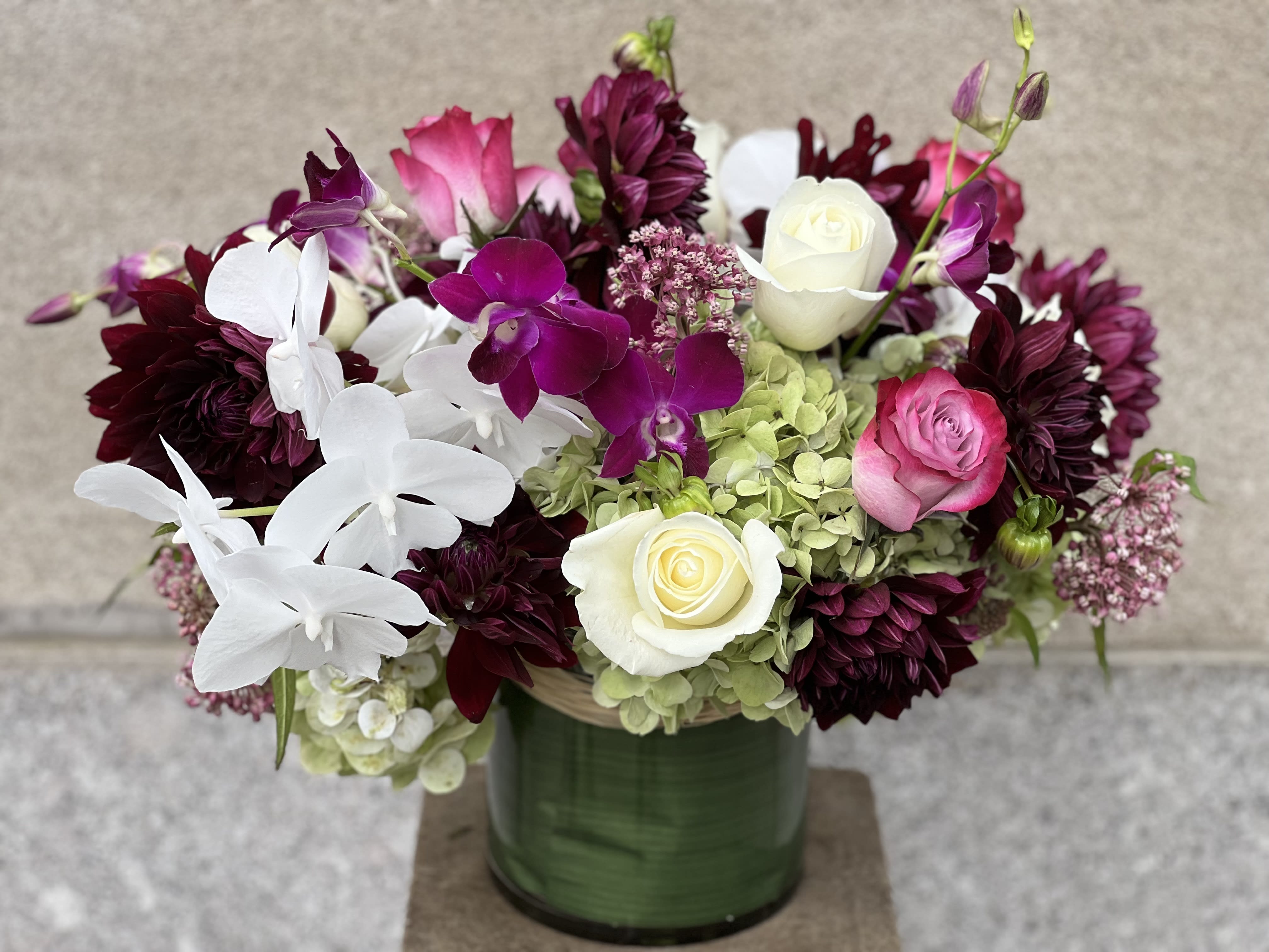 AUTUMN #3 - LUSH ASSORTMENT OF ROSES, PINK ASCLEPIAS, NUIT D'ETE DAHLIAS, WHITE PHALAENOPSIS ORCHIDS, BI - COLOR DENDROBIUM ORCHIDS   SET IN A LOW ROUND CYLINDER VASE. 