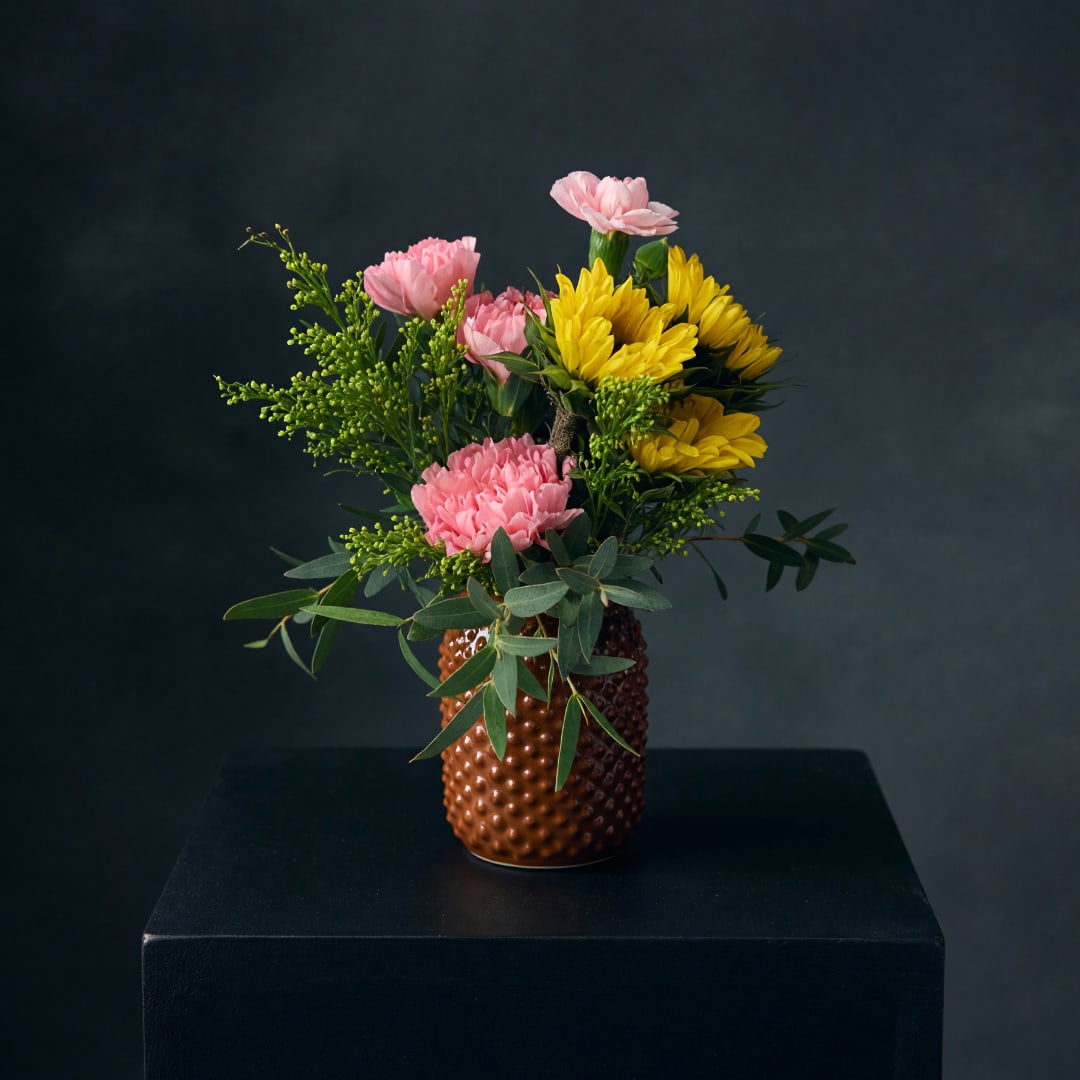 Pink and yellow flowers arranged in a textured brown vase
