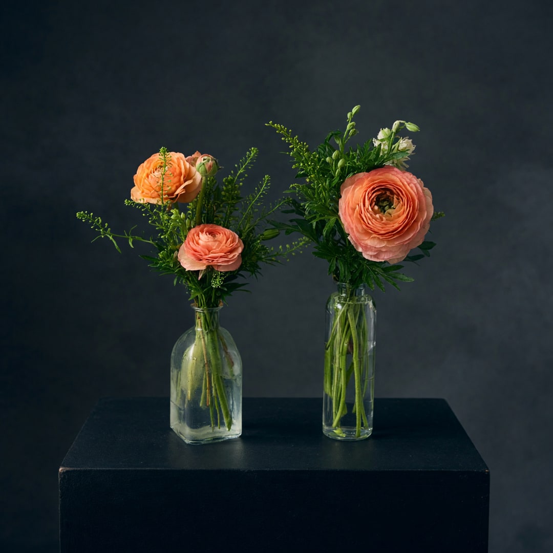 Two small floral arrangements in glass bottles with peach blooms