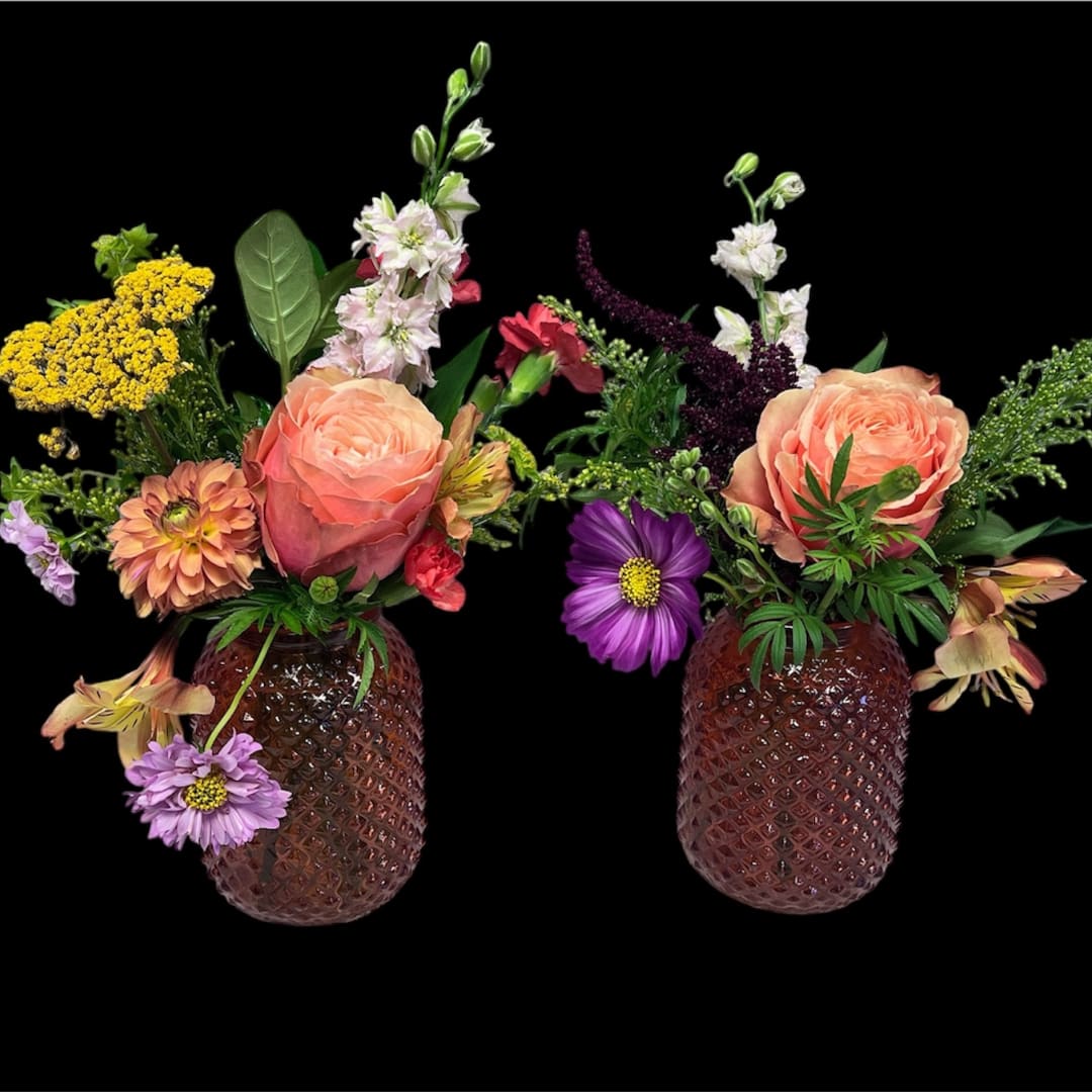 Two floral arrangements in textured brown vases with peach roses and mixed blooms