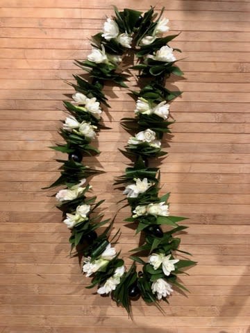 White floral lei with dark green leaves on a wooden floor