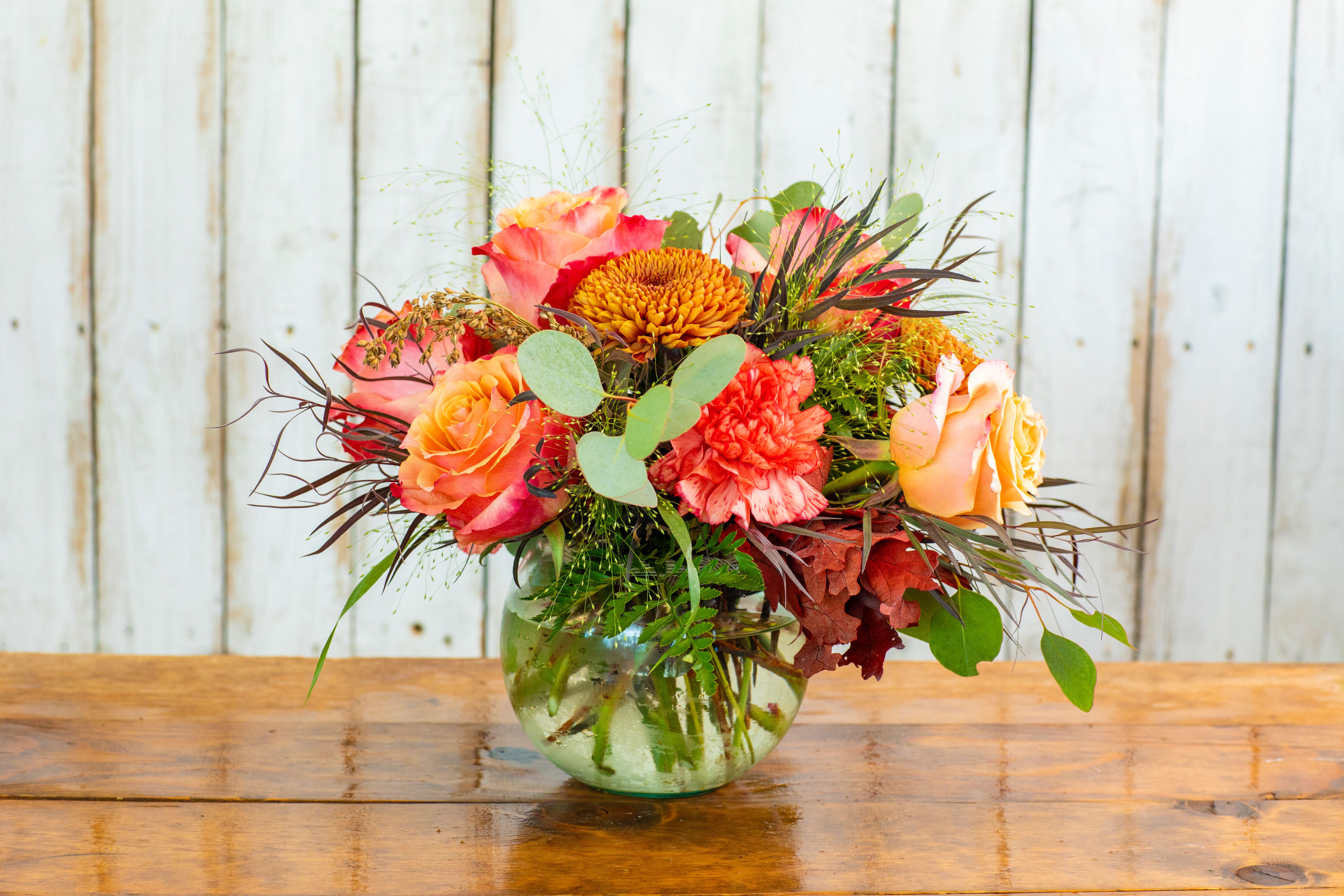 Mixed bouquet of orange, pink, and yellow flowers in a glass vase