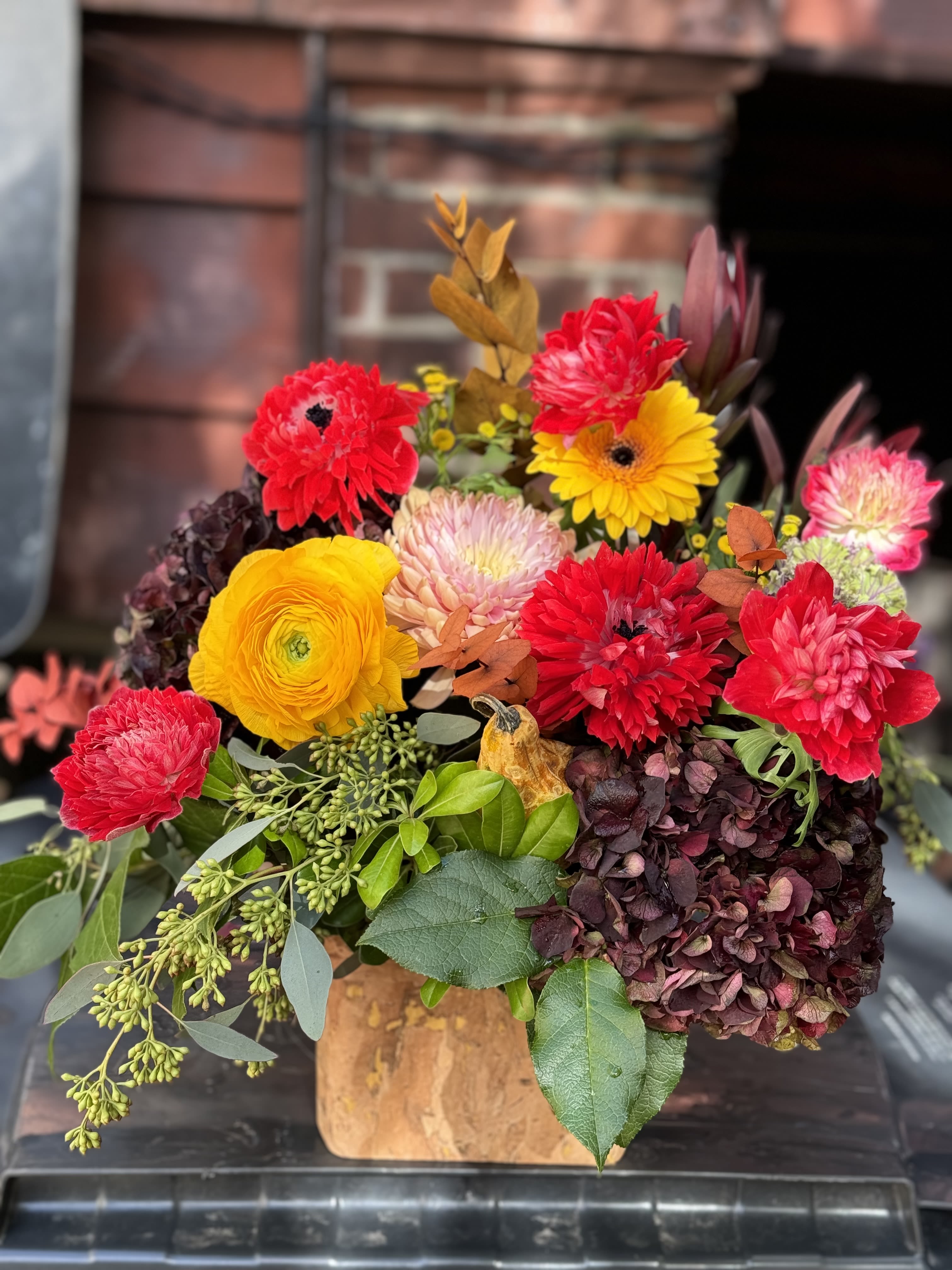 Bright mixed bouquet with red, yellow, and pink blooms in a wooden container