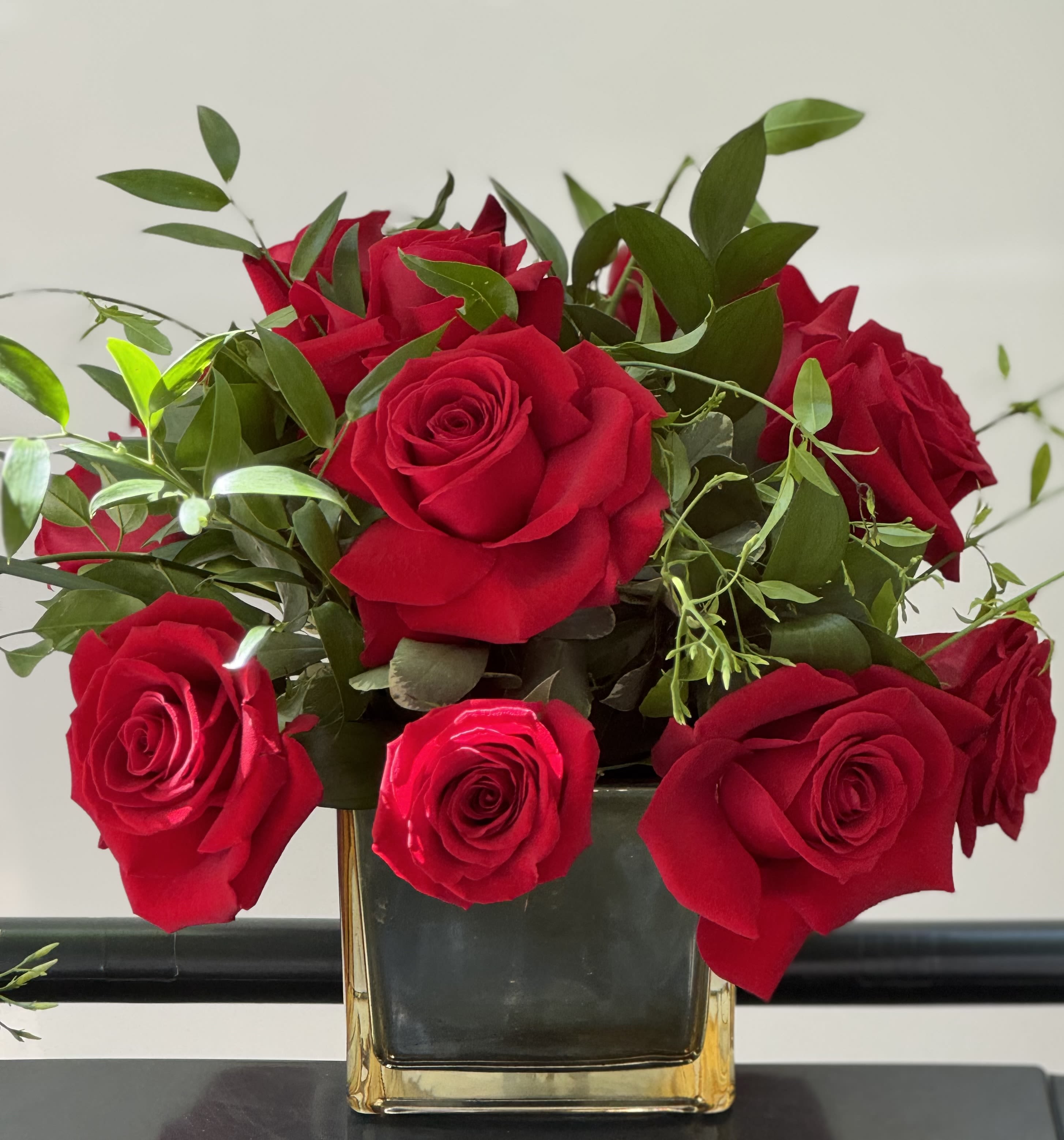 Red roses arranged in a square glass vase with greenery
