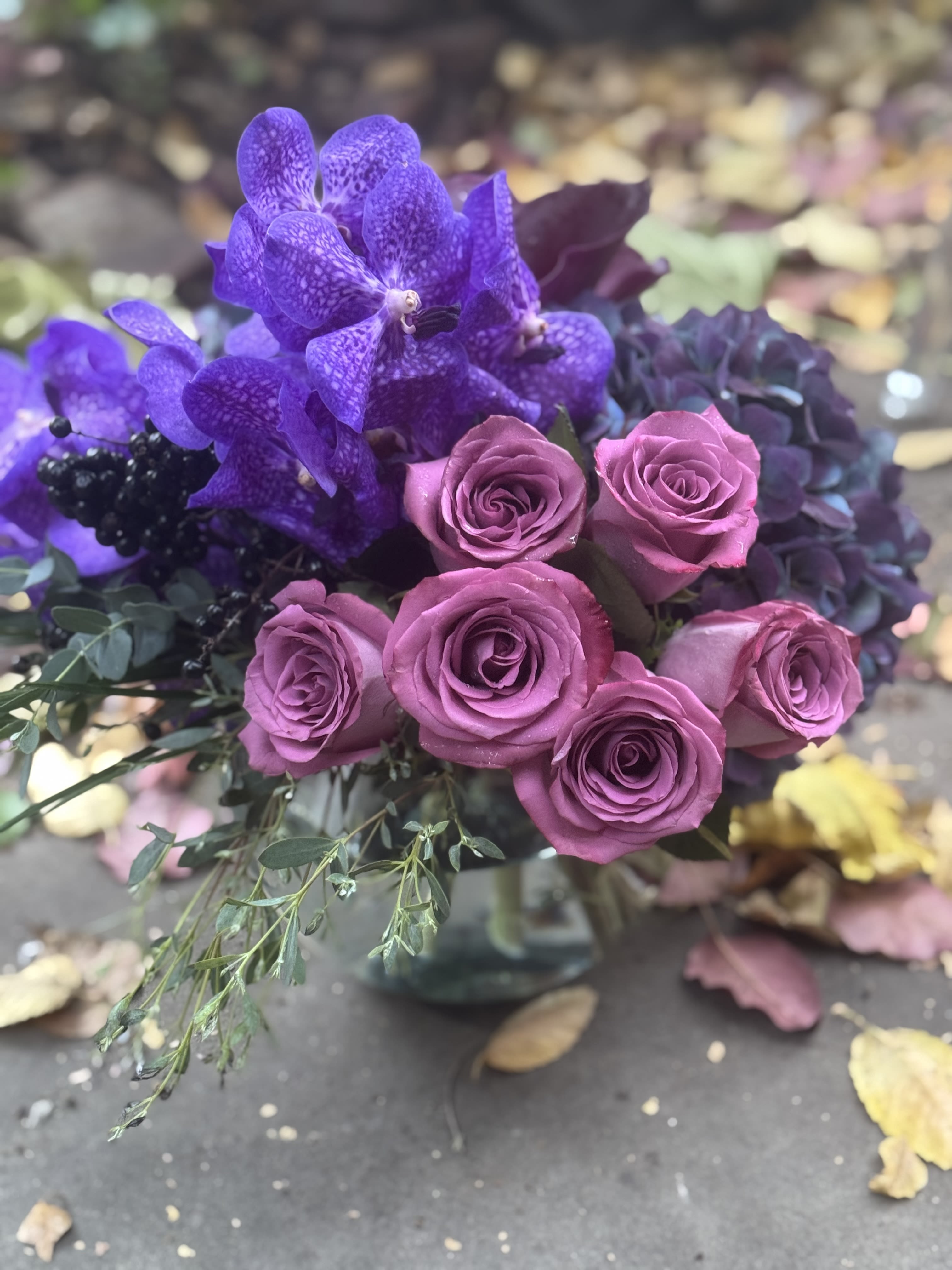 Purple orchids and pink roses arranged in a glass vase