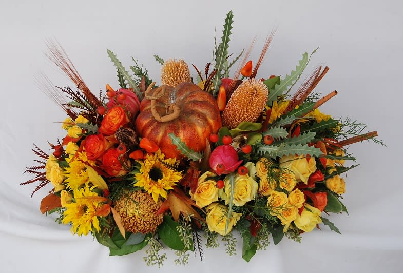 Fall Wishes Centerpiece  - A warm fall centerpiece with roses, sunflowers, peonies, pumpkin, rose hips, banksias, peppers, green cymbidium orchids, and bronze chrysanthemums is the perfect touch to any thanksgiving dinner table.    