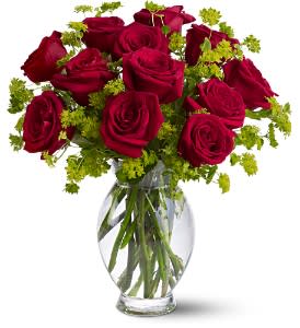 Red roses arranged in a clear glass vase with green filler