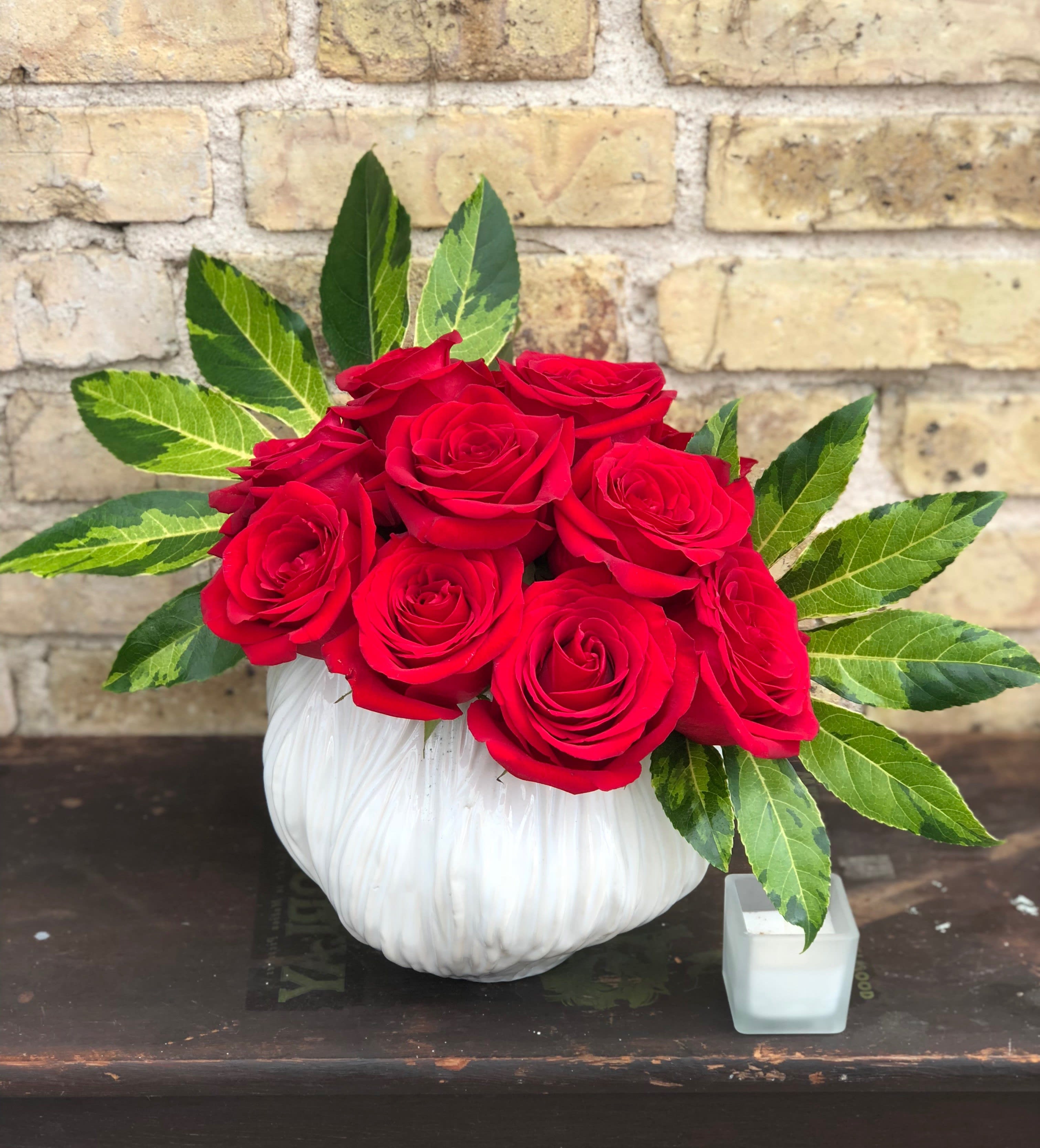 Red roses arranged in a white pumpkin-shaped vase with variegated leaves