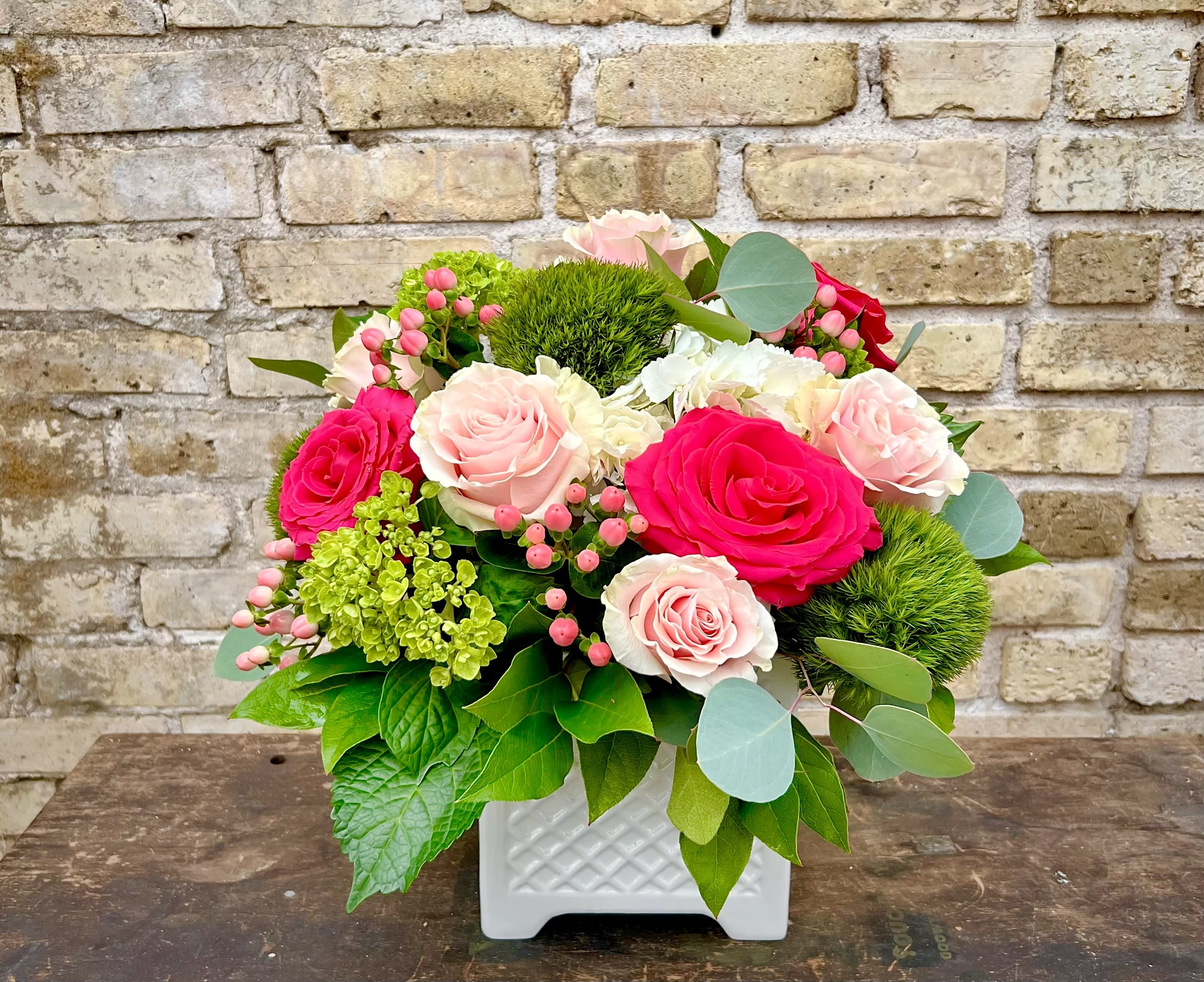 Pink and white roses in a white square vase with greenery